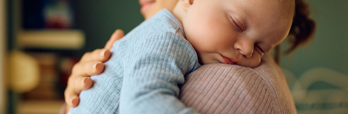 Bébé qui dort dans les bras de sa mère qui est debout.