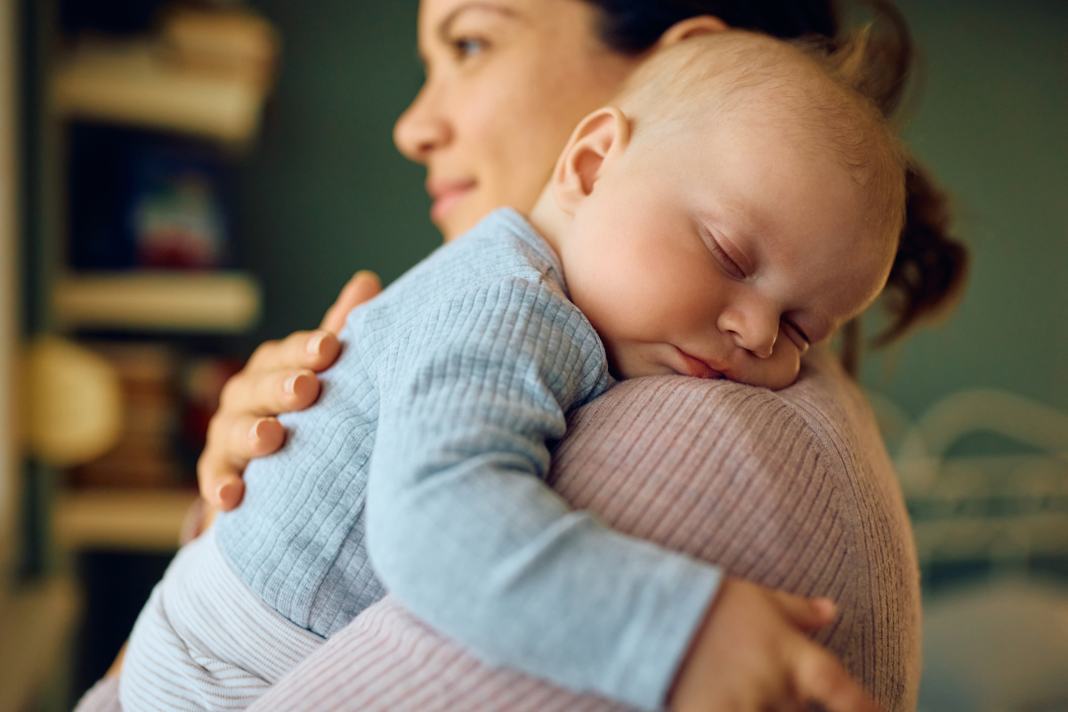 Bébé qui dort dans les bras de sa mère qui est debout.