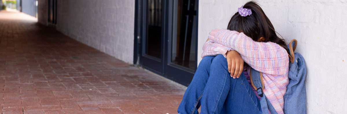 Adolescente en détresse, la tête dans les genoux, adossée au mur d'un bâtiment.