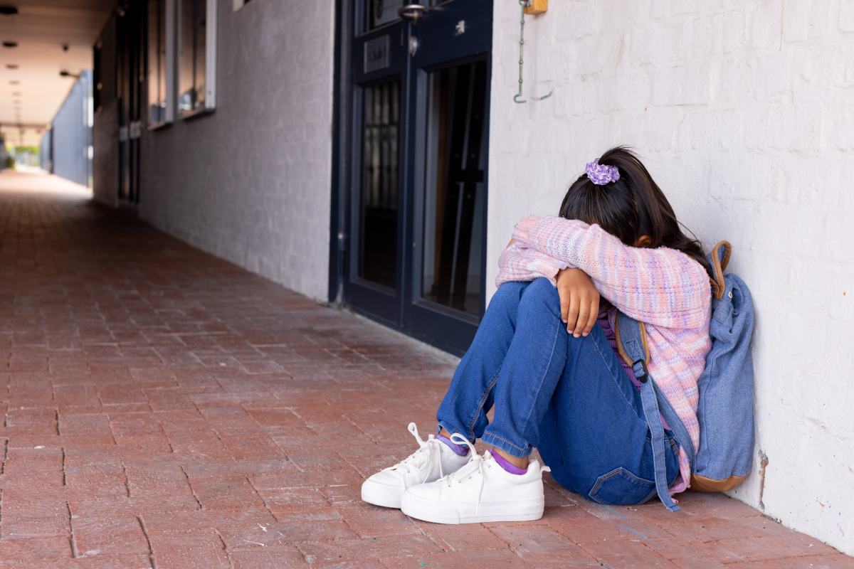 Adolescente en détresse, la tête dans les genoux, adossée au mur d'un bâtiment.